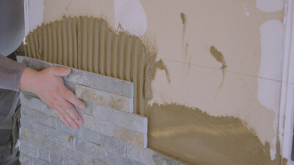 CLOSE UP: Builder presses a tile firmly against the wall covered in mortar.