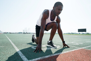 African american male sportsman ready to run on stadium track, sprint run from low start
