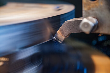 Close-up photo of metal machining on turning lathe. Lathe tool in focus, blank is motion-blurred. Low depth of field.