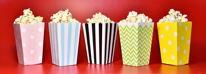 Popcorn in colored cardboard packaging. Heap of salted popcorn in paper striped bucketon a red background.