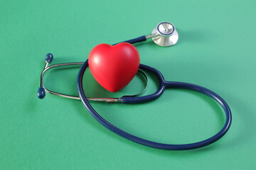 Medical stethoscope and heart on green background
