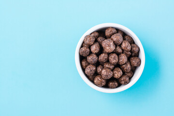 A bowl with cereal chocolate balls dry breakfast on a light blue background. Top view