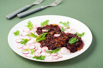 Vegetable diet food. Beetroot steak, radish and frize salad leaves on a plate on a green background