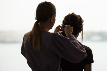 Silhouette of a hairdresser who makes a haircut to a girl-bride. Rear view in front of a large window.