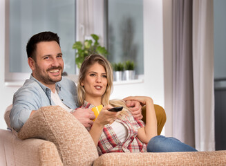 Attractive young couple sitting in living room watching tv