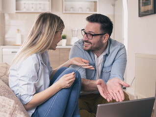 Young couple sitting on couch discussing shopping online using laptop