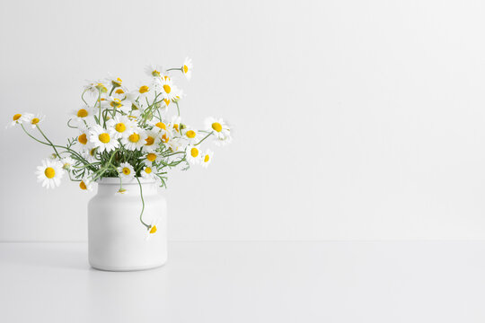 White chamomile flowers in vase on white table. Front view.
