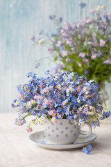 A bouquet of spring flowers forget-me-nots in a cup on the table against the background of a...
