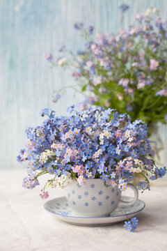 A bouquet of spring flowers forget-me-nots in a cup on the table against the background of a decorative colored wall. Postcard, blur, selective focus.