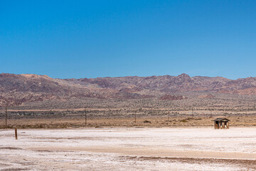 USA, CA, Salton Sea - December 28, 2012: SE shoreline with small ruinous shack isolated on whtie beach with mountains on horizon and blue sky above.