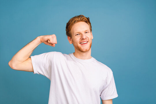 Portrait of a happy young man dressed in t-shirt showing biceps isolated over blue background.