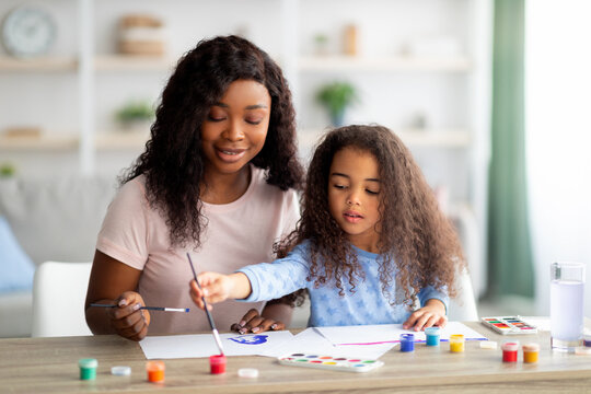Portrait of cheerful black mom and her daughter painting together, having artistic hobby at home. Family pastimes