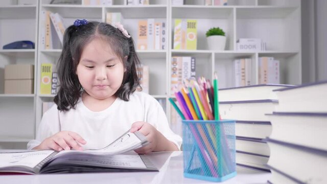 Beautiful inteligent young girl sat at home table reading  open book excited and happy resting head on hands