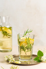 Homemade lemonade with elderflower syrup, lemon and sparkling water, in a glass. A pitcher with a...