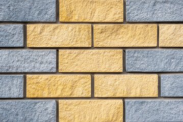 New building with textured wall of painted light grey and yellow colors stone blocks at bright light extreme close view
