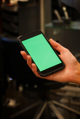 The human hand shows a mobile smartphone with a green screen in an upright position .Mock up mobile. blurred background