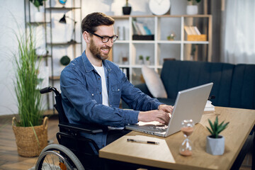 Young man with special needs in casual clothes and eyeglasses working on wireless laptop. Male...