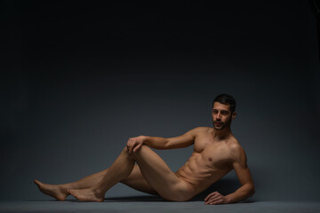 Fototapeta premium Gorgeous naked male model lying isolated on the floor in a studio while looking in the camera
