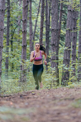 Young athletic sporty girl is jogging outside on a forest path