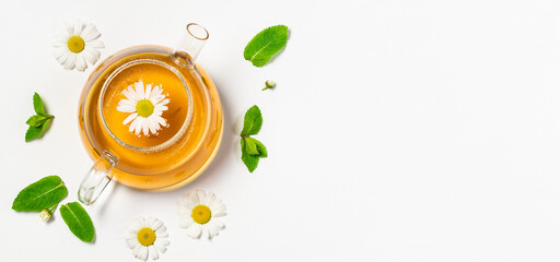 Glass kettle with herbal chamomile and mint tea on white background top view. Long banner format....
