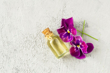 Glass bottle of essential pansy oil with fresh violet flowers, beauty treatment, alternative medicine