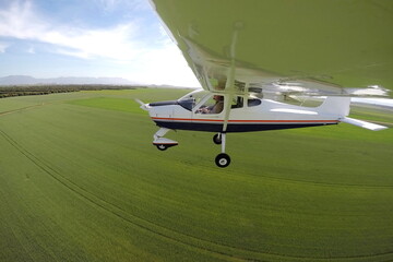 PILOT IN A PLANE FLYING OVER GREEN FIELDS
