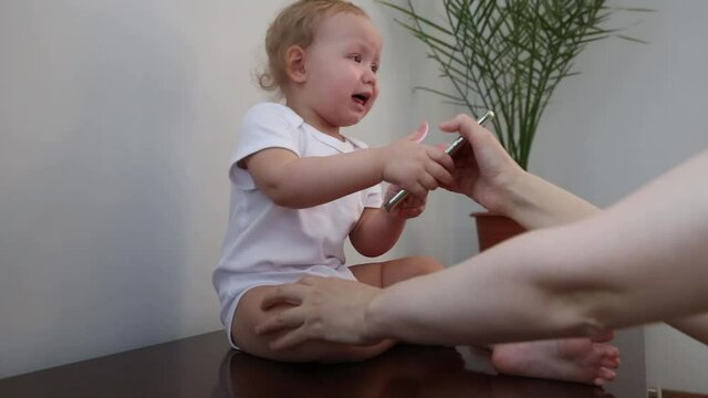 The mother's hand takes the mobile phone from the child. Toddler cries and demands the phone. Mobile addicted child