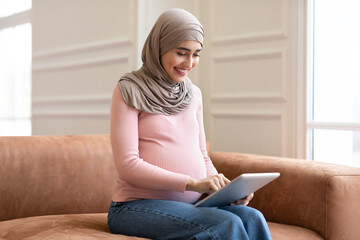 Side View Of Pregnant Muslim Female Using Tablet At Home