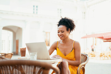 Student learning during a break on a laptop. Sitting in a summer restaurant ordered breakfast before work. Young woman shopping online in a cafe.