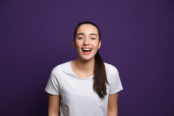 Beautiful young woman laughing on purple background. Funny joke