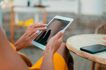 Uses a new gadget in a summer cafe watching the news. A woman holds a tablet in her hands to surf the Internet. Beautiful color yellow dress.