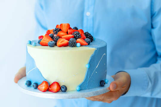  A man pastry shef holding a beautiful big cake with berries in his hands. Male chef cook confectioner or baker. Mock up copy space food concept. Cake sales and stores. birthday cake