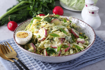 Salad with cabbage, radishes, parsley, green onions and eggs, seasoned with sour cream on a gray background. Healthy food