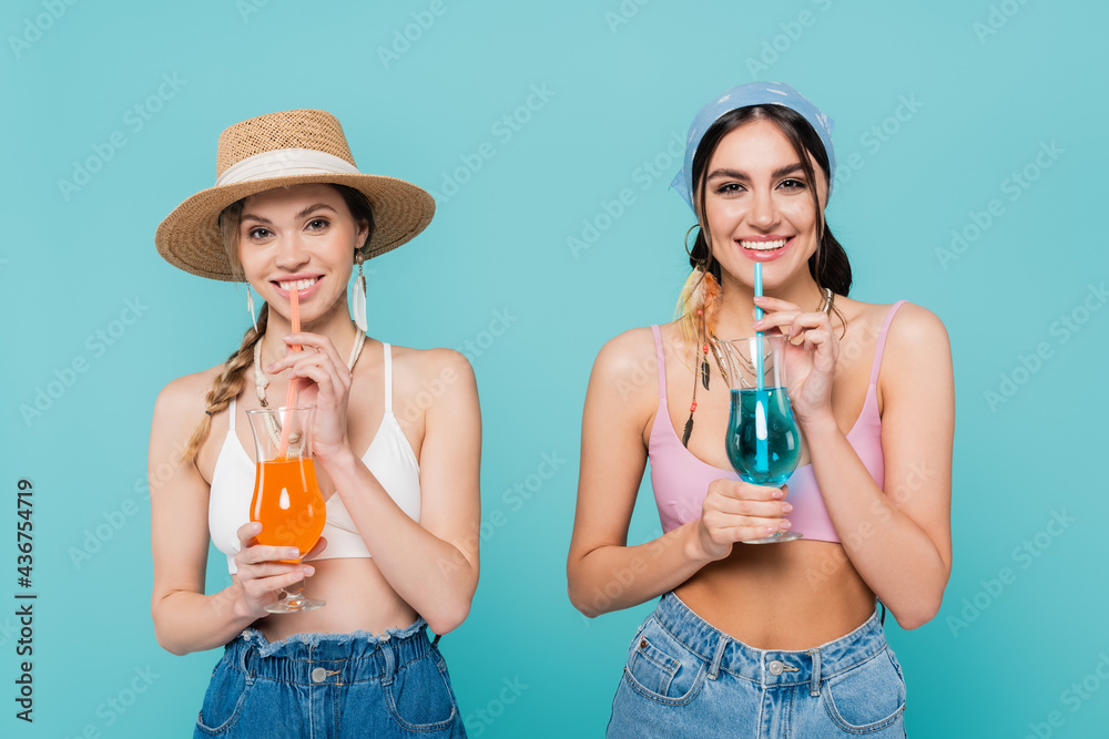 Wall mural pretty women with cocktails looking at camera isolated on blue.