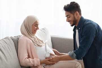 Loving Arab Husband Placing Wireless Headphones On Pregnant Wife's Belly