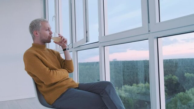 Slow motion shot af a young european guy drinking wine at the balcony enjoying the view and the sunset. High quality 4k footage
