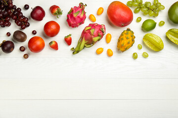 Many different delicious exotic fruits on white wooden table, flat lay. Space for text