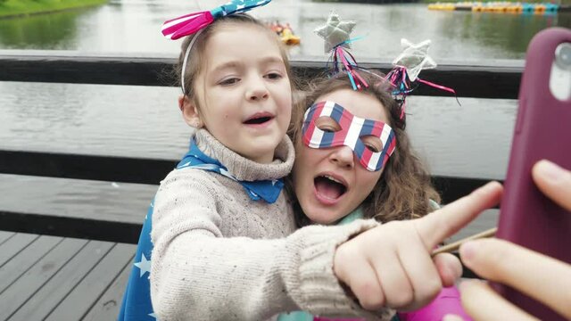 Close up. Cute girl and woman wear symbols usa national flag, happily talk in video conference by smartphone together, celebrating 4th of July. Activity technology lifestyle mobile phone use concept