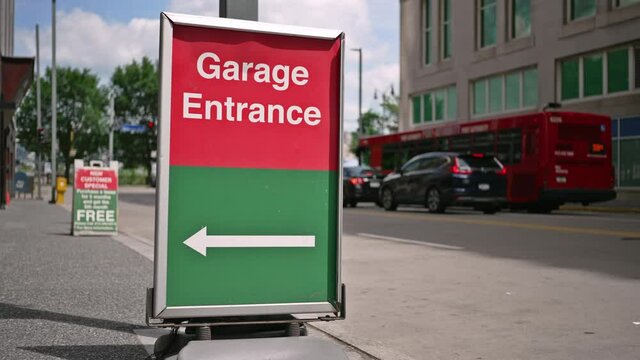 A stationary view of a parking garage entrance sign on a city sidewalk on a sunny summer day.	