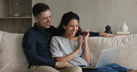 Hispanic millennial married couple sit on sofa using laptop making video call. Spend weekend communicating with friends, family living abroad remotely. Virtual meeting, videoconferencing event concept