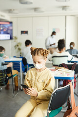 Vertical portrait of cute girl wearing mask in school and using smartphone, covid safety measures, copy space