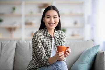 Cheerful asian lady drinking coffee in living room