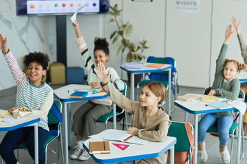Diverse group of happy children raising hands in school classroom, copy space