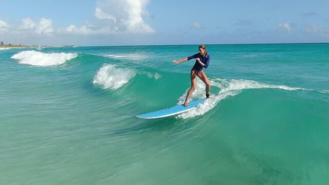Young woman is surfing on the light blue waves of the ocean, sports