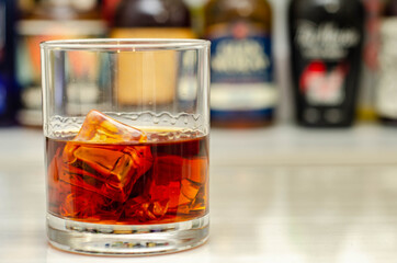 Old fashioned glass with scotch whisky and ice cubes on the bar