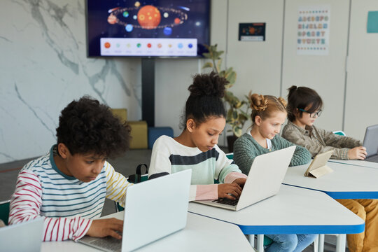Diverse group of children sitting in row at school classroom and using computers - Powered by Adobe