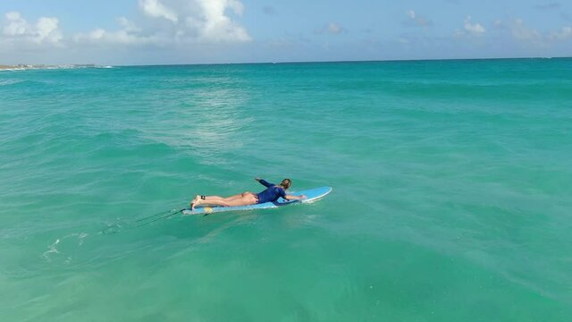Woman is lying on a surfboard and swimming in the ocean, light blue water