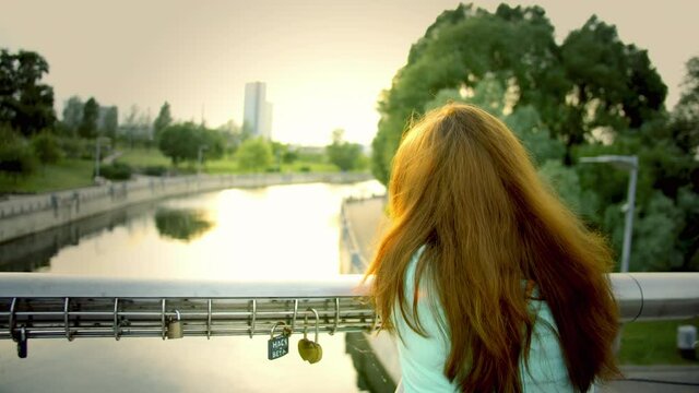 Woman at the meeting place with her beloved, breakup, failed relationship, unfinished love, brunette woman alone stands on the bridge at sunset on a summer day