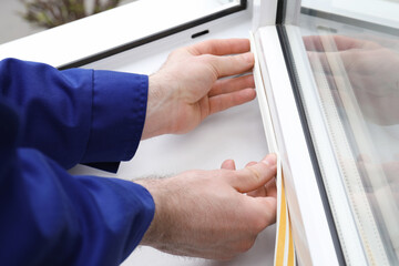 Worker putting rubber draught strip onto window indoors, closeup - obrazy, fototapety, plakaty
