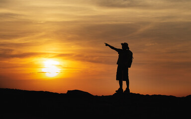 Silhouettes of hiker man with backpack enjoying sunset view from top of mountain.